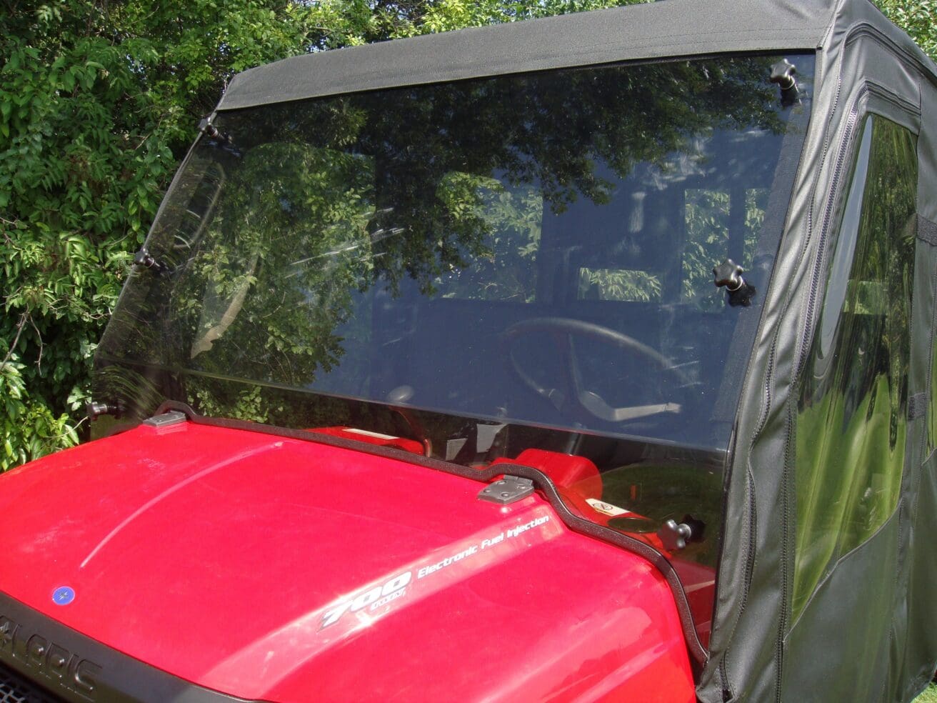 A red vehicle with a black windshield and some trees