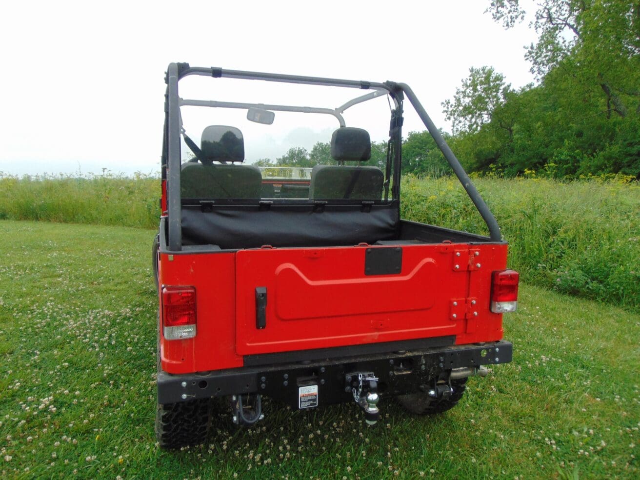 Red jeep with black roll bar in field.