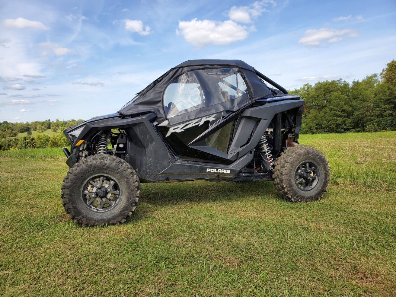 Black Polaris RZR in grassy field.