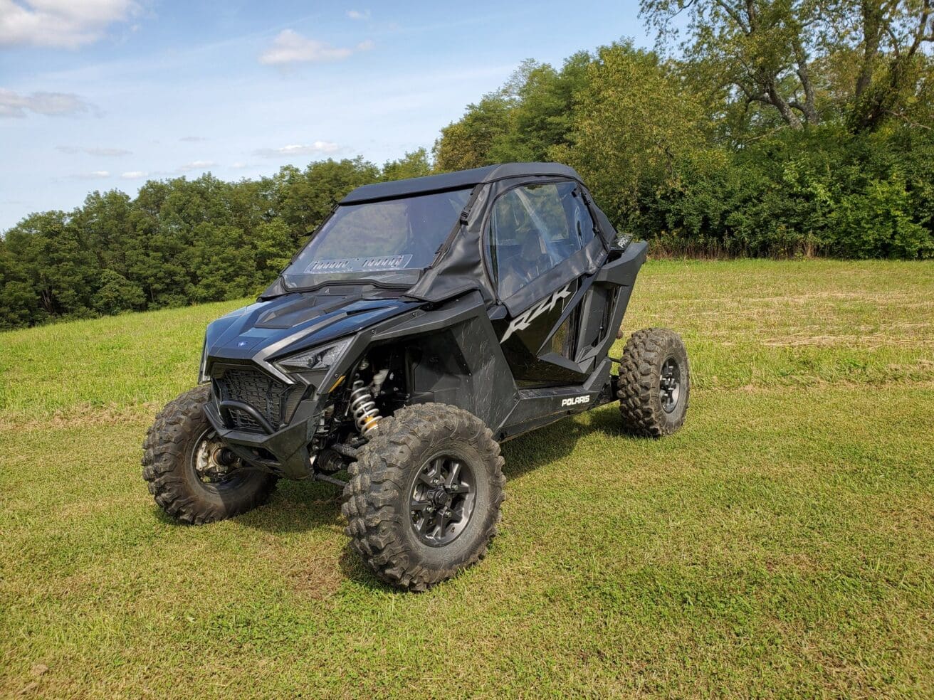 Black Polaris RZR in grassy field.