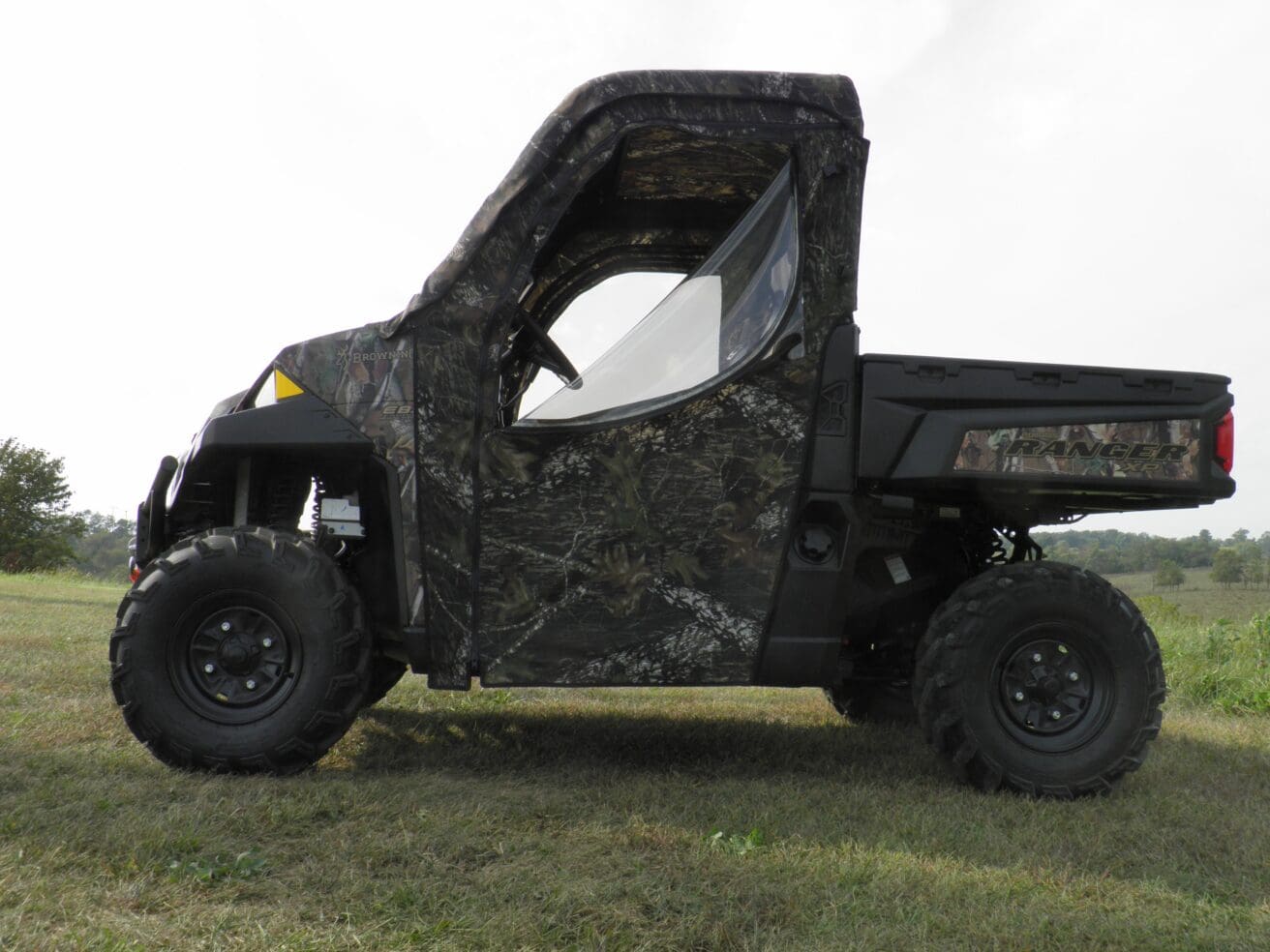 Camouflage utility vehicle parked on grassy terrain.