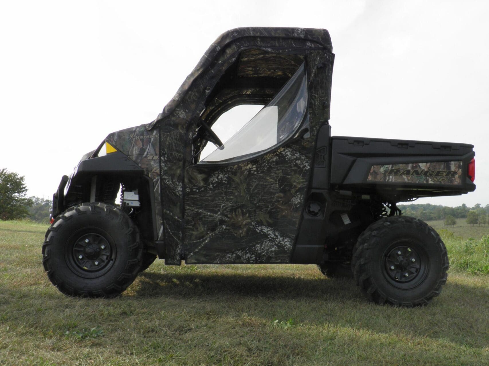 Camouflage utility vehicle parked on grassy terrain.